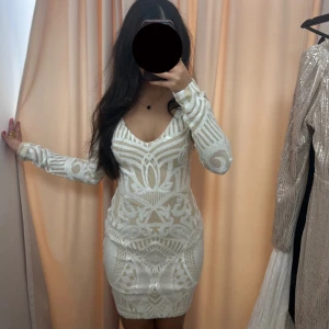 Vit glittrig kortklänning med mönster - Supersnygg vit kortklänning med glittriga detaljer och unikt mönster. Klänningen har lång ärm, v-ringning och figurnära passform. Klänningen finns i alla storlekar XS-XL ,                 Pris går att diskutera!