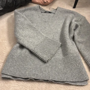 Grå stickad tröja från BikBok - Mysig grå stickad tröja från BikBok med v-ringning och breda ribbade muddar vid ärmslut och nederkant. Tröjan har slits på sidan. Skriv vid frågor💕