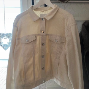 Beige manchesterjacka från Monki - Säljer en beige manchesterjacka från Monki i klassisk jeansjackemodell. Jackan har krage, knäppning framtill med silvriga knappar och två bröstfickor med lock. Perfekt för dig som gillar en stilren och trendig look.