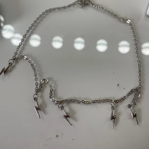 Silverhalsband med blixtar - Snyggt halsband i silverfärgad metall med flera små blixtformade berlocker längs kedjan. Kedjan är tunn och smidig, perfekt för att ge en cool touch till din outfit. Blixtarna hänger jämnt fördelade och ger ett edgy intryck. Ej riktigt silver