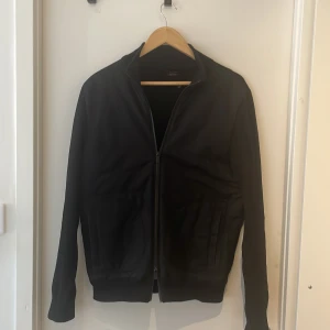 Svart cardigan från Massimo Dutti - Svart cardigan från Massimo Dutti i extrafin bomull. Jackan har dragkedja framtill, ståkrage och två fickor på sidorna. Enkel och stilren design som passar perfekt till många olika outfits.