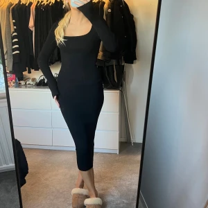 Svart ribbad långklänning - Snygg svart långklänning med ribbad struktur och lång ärm. Klänningen har en fyrkantig urringning och sitter tight mot kroppen för en slim och stilren look. Perfekt för dig som gillar minimalistisk och trendig stil.