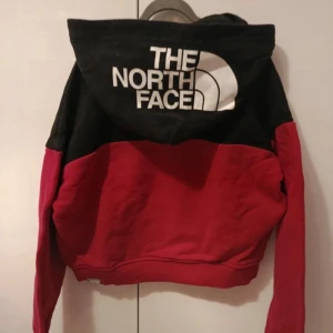 hoodie från The North Face- Unisex - str S/M - Säljer en snygg hoodie från The North Face i rött och svart med stor logga på huvan. Tröjan har en klassisk passform, långa ärmar och är tillverkad i mjuk bomullsmix. Perfekt för dig som gillar streetwear och vill ha något bekvämt och stilrent. Unisex str S/M