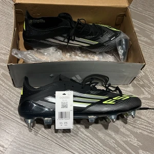 Adidas F50 Elite svarta fotbollsskor - Adidas F50 fotbollsskor i svart med vita och neongula detaljer. Skorna har snörning, spetsig tå och metall-dobbar för extra grepp på planen. Snyggt mönster med F50-tryck och klassiska Adidas-ränder på sidan. Ovandelen är tillverkad i syntetmaterial för lätt känsla. Hör av er vid frågor
