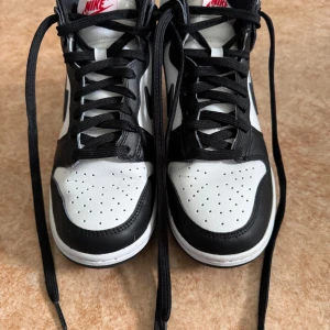 Nike Dunk High svartvita sneakers - Svartvita Nike Dunk High sneakers med klassisk design och högt skaft i storlek 38. Skorna är normala i storlek och har bara använts några fåtal gånger. 