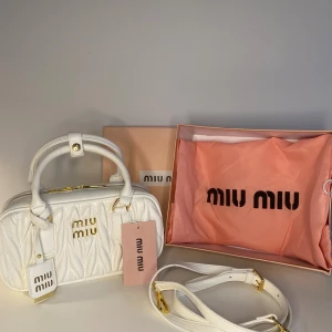 Vit quiltad handväska från Miu Miu - Superfin vit handväska från Miu Miu i quiltat skinn med guldiga detaljer och logga framtill. Väskan har både handtag och avtagbar axelrem, perfekt för att bära på olika sätt. Kommer med originalbox och dustbag. Snygg och lyxig accessoar som lyfter varje outfit.