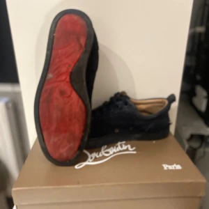  Christian Louboutin - Säljer ett par svarta sneakers från Christian Louboutin med klassisk röd sula. Skorna har rund tå, snörning och är tillverkade i mocka med svarta detaljer. Innersulan är beige och de kommer med originalkartong och dustbag.                                          Bara att skriva vid frågor och funderingar.  Priset är ej hugget i sten 