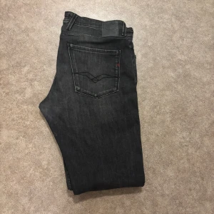 Replay svarta jeans, modell Anbass - Säljer ett par svarta Replay Anbass jeans. Jeansen har en slim passform med raka ben och snygga slitningar framtill. Materialet är mjukt och stretchigt jeans, perfekt för en modern look. Hör av er vid frågor!