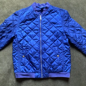 Quiltad blå bomberjacka Polo Ralph Lauren - Snygg quiltad bomberjacka från Polo Ralph Lauren i en djup blå färg. Jackan har ribbade muddar. Nypris 2500kr