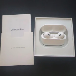 AirPods Pro 2 - Apple AirPods Pro i originalförpackning med laddningsetui, extra öronproppar och laddkabel. Komplett med manual. Hörlurarna ser ut att vara i mycket gott skick, inga synliga repor eller skador. Perfekt för brusreducering och trådlös musikupplevelse.