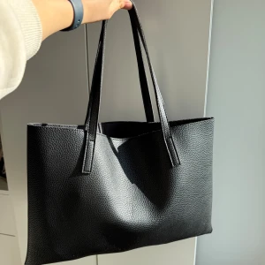 Vince Camuto svart handväska i skinn. Använ 1 gång. Som ny - •En gång använd stilren svart handväska med långa handtag.  •Väskan har en strukturerad yta och en avskalad design.  •Perfekt för att bära dina vardagliga ägodelar med stil. •Äkta läder •Köpte i Milano •Djur och rökfritt hem