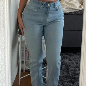 Ljusblå raka jeans med hög midja - Säljer ett par ljusblå jeans med hög midja och raka ben. Jeansen har klassisk femficksdesign, knapp- och dragkedjestängning samt bälteshällor. 