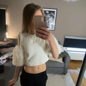 Vit croppad topp med fluffiga ärmar - Säljer en vit croppad topp med ribbad struktur och unika fluffiga ärmar. Toppen är ärmlös upptill med offshoulder-design och har en cool, modern look. Perfekt för dig som vill sticka ut med en trendig och annorlunda stil.
