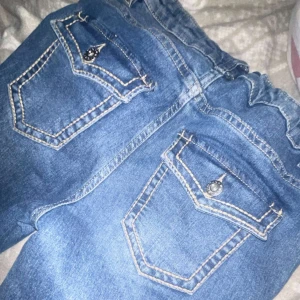 Blå jeans med detaljerade fickor - Snygga blå jeans med kontrasterande vita sömmar och två bakfickor med lock och dekorativa knappar. Jeansen har klassisk femficksdesign och är perfekta för dig som gillar coola detaljer på dina byxor.