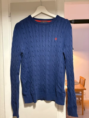 Blå Kabelstickad tröja från Morris S - Blå kabelstickad tröja med rund hals och lång ärm. Väldigt bra passform och mycket skön att bära. Tröjan är använd och ganska urtvättad, vilket syns något i färgen, men fortfarande i fullt brukbart skick. Passar perfekt till vardagligt bruk. 