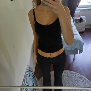 Svarta bootcut-byxor från Gina Tricot - Säljer ett par svarta bootcut-kostym byxor från Gina Tricot med låg midja. Byxorna har två knappar och dragkedja framtill samt fickor bak med knappdetalj. Materialet är mjukt, vilket gör dem riktigt sköna och snygga att bära. Perfekta för dig som gillar en klassisk och stilren look. 