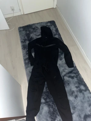 En svart nike tracksuit  - Svarta mjukisbyxor från Nike med dragsko i midjan och logga på benet. Byxorna har en loose passform och är tillverkade i mjukt bomullsmaterial. Perfekta för chill eller träning, med klassisk stil och bekväm känsla.