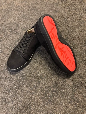 Christian Louboutin svarta sneakers - Svarta sneakers från Christian Louboutin med ikonisk röd sula och snygg signatur. Skorna har snörning, rund tå och är tillverkade i mocka och skinn. Kommer med originalkartong, dustbag och äkthetskort. Perfekt för dig som vill sticka ut med exklusiv stil.