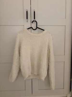 Fluffig vit stickad tröja med hål i ryggen - Supermjuk och fluffig vit stickad tröja med lång ärm och rund hals. Baksidan har en snygg öppen detalj med knapp upptill. 