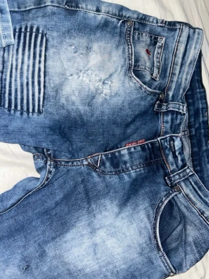 Blå Dsquared jeans med ribbade detaljer - Säljer ett par blå jeans från Dsquared2 med coola ribbade detaljer på både fram- och bakfickor. Jeansen har en tvättad look med ljusare partier. Snygga kontrastsömmar och logga på bakfickan ger extra stil. Inte så använda, men i helt ok skick — därav priset. Pris kan diskuteras!