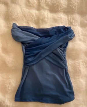 Blå omlott offshoulder topp från Pull & Bear, XS - Säljer en snygg blå omlott topp med offshoulder-design. Toppen har ett draperat tyg som korsas över bröstet. Materialet är mjukt och stretchigt.