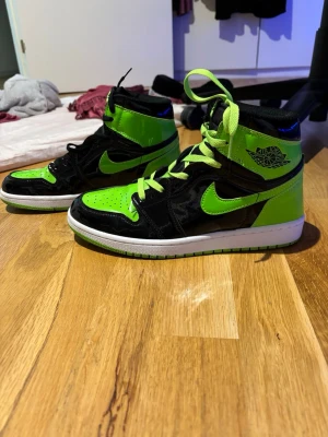Nike Air Jordan 1 High Svart/Neongrön - Säljer ett par Nike Air Jordan 1 High sneakers i svart och neongrönt lackat skinn. Skorna har klassisk Jordan-logga på sidan, perforerad tå och kontrasterande svarta och gröna skosnören. Vit sula med grön detalj undertill. Riktigt eye-catching och perfekta för dig som vill sticka ut.