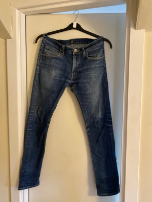  jeans från Lee - Snygga blå jeans från Lee med klassisk femficksdesign och skinny passform. Jeansen har en mörk tvätt med lätt slitning och Lee-logga på bakfickan. Perfekt för dig som gillar en smal siluett och tidlös stil.
