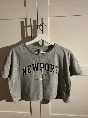 Grå croppad t-shirt strl. S - En lite använd croppad t-shirt med Newport tryck på framsidan.