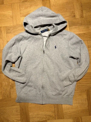 Polo Ralph Lauren Grå sip hodie - Tja säljer en grå polo sip hodie, i storlek M. Har inga defekter förutom en knappt syn bar Fläk på höger sida av sipen. Passar perfekt till alla tillfällen för en stilren look. Vid minsta fråga är det bara att höra av sig.
