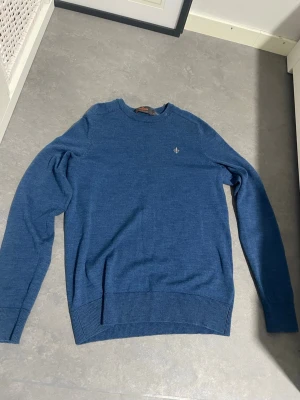 Blå stickad tröja från Morris - Snygg blå stickad tröja från Morris med rund hals och diskret logga broderad på bröstet. Tröjan har ribbade muddar vid ärmslut och nederkant, vilket ger en schysst passform. Perfekt för dig som gillar stilrena och klassiska plagg. Hör av er vid frågor!😊