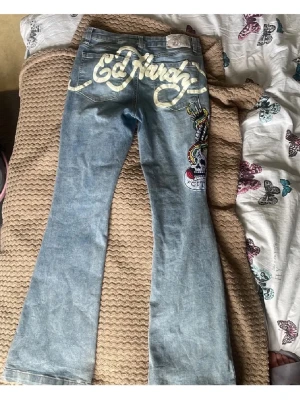 Ed Hardy jeans med tryck och brodyr - Snygga ljusblå jeans från Ed Hardy med stort gult logotryck över bakfickorna och färgglad broderad dödskalle och orm längs benet. Klassisk femficksmodell i denim med utsvängda ben och cool streetstil.