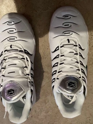 Nike Air Max vita sneakers - Nike Air Max sneakers i vitt med svarta grafiska detaljer och inslag av grönt på sidan. Skorna har synlig Air Max-dämpning i sulan, snörning och en cool silverdetalj på plösen. Materialet är syntet och mesh för en fräsch och sportig look.