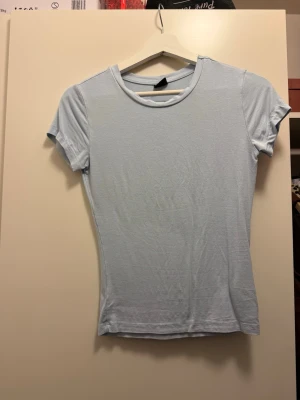 Ljusblå t-shirt från Gina Tricot XS - Snygg ljusblå t-shirt från Gina Tricot i storlek XS. Modellen är klassisk med rund hals och korta ärmar, perfekt för en chill och enkel look. Materialet är mjukt och känns skönt mot huden, t-shirten har en slim passform som sitter snyggt.