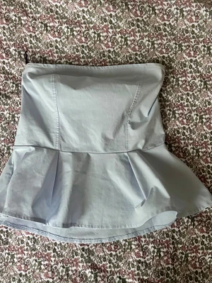 Ljusblå volang tubtopp - Säljer en ljusblå tubtopp med volang nertill. Toppen är axelbandslös och har en figurnära passform upptill som går ut i en snygg volang. Perfekt för dig som vill ha en trendig och passar alla årstider