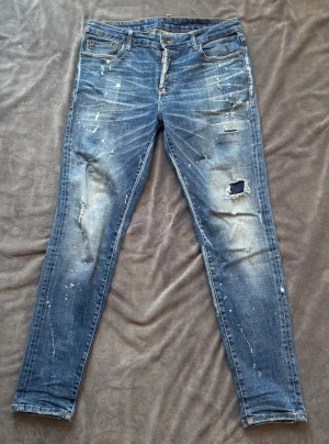 Dsquared2 skinny jeans med slitningar - Säljer ett par blå jeans från Dsquared2 med snygga slitningar, hål och färgstänk.