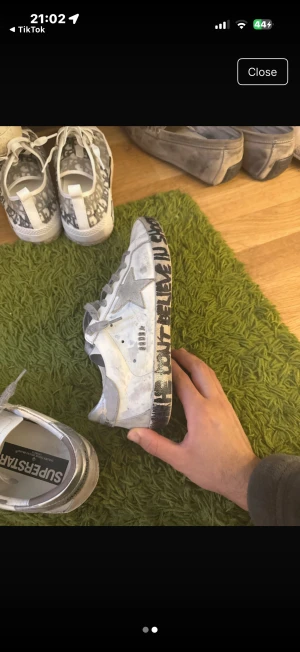 Golden Goose Superstar sneakers vit/grå - Golden Goose Superstar sneakers i vitt skinn med grå detaljer och silverfärgad stjärna på sidan. Sulan har handskriven text i svart och skorna har grå snörning. Platt sula och rund tå. Snyggt sliten look som ger extra edge till outfiten.