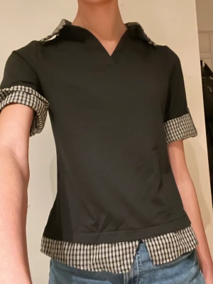 Svart topp med rutiga detaljer -  svart topp med rutiga detaljer i svart vitt. Toppen har korta ärmar och en v-ringad hals. Är i storlek m, jag har storlek xs/s. Har bara provats en gång. 