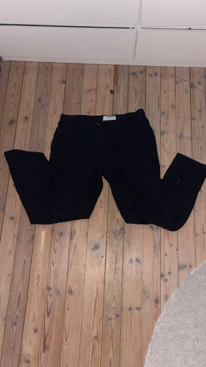 Svarta linnebyxor från Only & sons - Svarta byxor från Only & Sons med avslappnad passform och snörning i midjan. Modellen har raka ben, sidofickor och bakfickor med knapp. Perfekta för en chill och stilren look. Funkar bra till sommaren och lätt att matcha med andra plagg. Tveka inte att höra av dig vid intresse eller möjliga frågor!