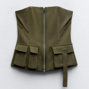 Olivgrön bandue topp - Säljer en olivgrön bandue topp, med fickor på framsidan. Väldigt snygg med en dragkedja i mitten.