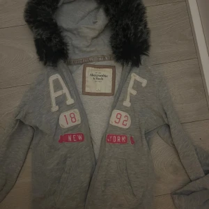 Fur hoodie zip up Abercrombie & Fitch - Säljer en grå zip up från Abercrombie & Fitch med fluffig svart päls på luvan som är påsydd mycket bra av oss.