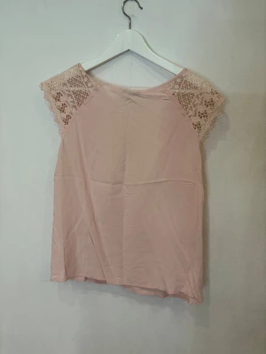 Ljusrosa blus med spetsärmar från My hoilys  - Supersöt ljusrosa blus från Mirrack med ärmlös design och vackra spetsdetaljer på axlarna. Blusen har rund halsringning och ett flowy fall, perfekt för en chill och feminin look. Materialet känns lätt och luftigt.