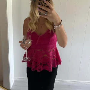 Rosa spetsig linnetopp med volang - Säljer en snygg rosa linnetopp med spetsdetaljer och volang nertill. Toppen har smala axelband, v-ringning och är genombruten med blommigt spetsmönster. Perfekt för dig som vill sticka ut med en feminin och trendig look.