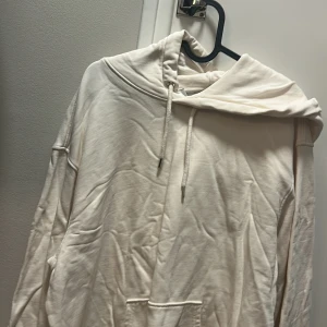 Vit hoodie med huva och snörning - Säljer en stilren vit hoodie med huva och snörning. Tröjan har en klassisk känguruficka framtill och långa ärmar. Perfekt för dig som gillar en enkel och clean look. Passar dig som vill ha en bekväm och avslappnad stil.