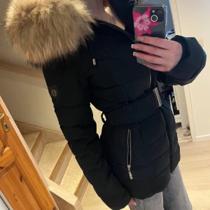 Svart pufferjacka med päls från Hollies - Säljer en varm pufferjcaka från Hollies med stor fluffig päls på huvan och snygga guldfärgade dragkedjor. Jag har använt den i en vinter, jag är 166 cm lång 🌸🌸