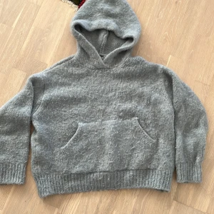Grå stickad hoodie från Zara - Mysig grå stickad hoodie från Zara med stor huva och magficka. Tröjan har ribbade muddar vid ärmslut och nederkant, vilket ger en chill och avslappnad vibe. Perfekt för kalla dagar när du vill vara både bekväm och snygg.