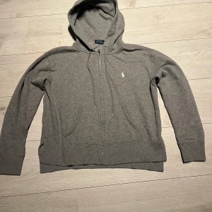  Ralph Lauren hoodie - En snygg Ralph Lauren hoodie i färgen grå. Den har ett litet håll som ni kan se på bilden annars jätte fin, därför detta pris 