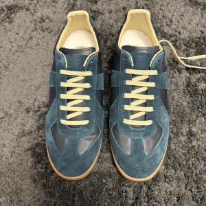 Nya Mörkblå sneakers från Maison Margiela - Maison Margiela sneakers i mörkblå mocka och skinn med beige snörning och gummisula. Klassisk rund tå och platt sula, stilren design med kontrasterande material och färger. Kommer med vit låda och dustbags. Perfekt för dig som gillar exklusiva och trendiga sneakers. Kvitto finns, bara att fråga, ytterligare frågor är bara att höra av sig.