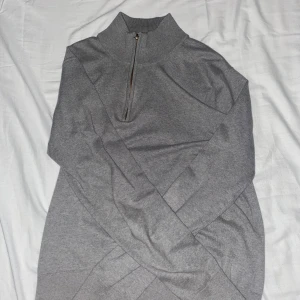 Grå stickad half zip tröja GRUNT XL - Snygg grå stickad tröja från GRUNT i storlek XL. Tröjan har en hög krage och half zip-dragkedja framtill. Perfekt för dig som gillar enkel och clean stil. Materialet är mjukt och ribbat vid krage och muddar. Passar dig som vill ha en chill och stilren look.