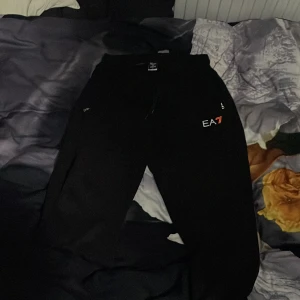 Svart mjukis sett från EA7 Emporio Armani - Svarta mjukisbyxor från EA7 Emporio Armani med dragsko i midjan och logga på vänster ben. Byxorna har en avslappnad passform och är perfekta för chill eller träning. Tillverkade i mjukt material för maximal komfort. storlek XL men har passform i M