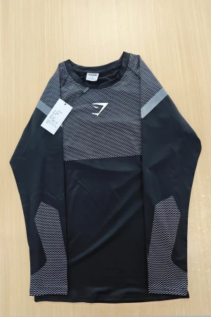 Svart långärmad träningströja Gymshark - Svart långärmad träningströja från Gymshark i storlek S. Tröjan har coola grå och vita detaljer med ett randigt mönster på axlar och ärmar samt Gymshark-logga på bröstet. Tillverkad i mjukt och stretchigt polyester-material som andas bra under träningen.